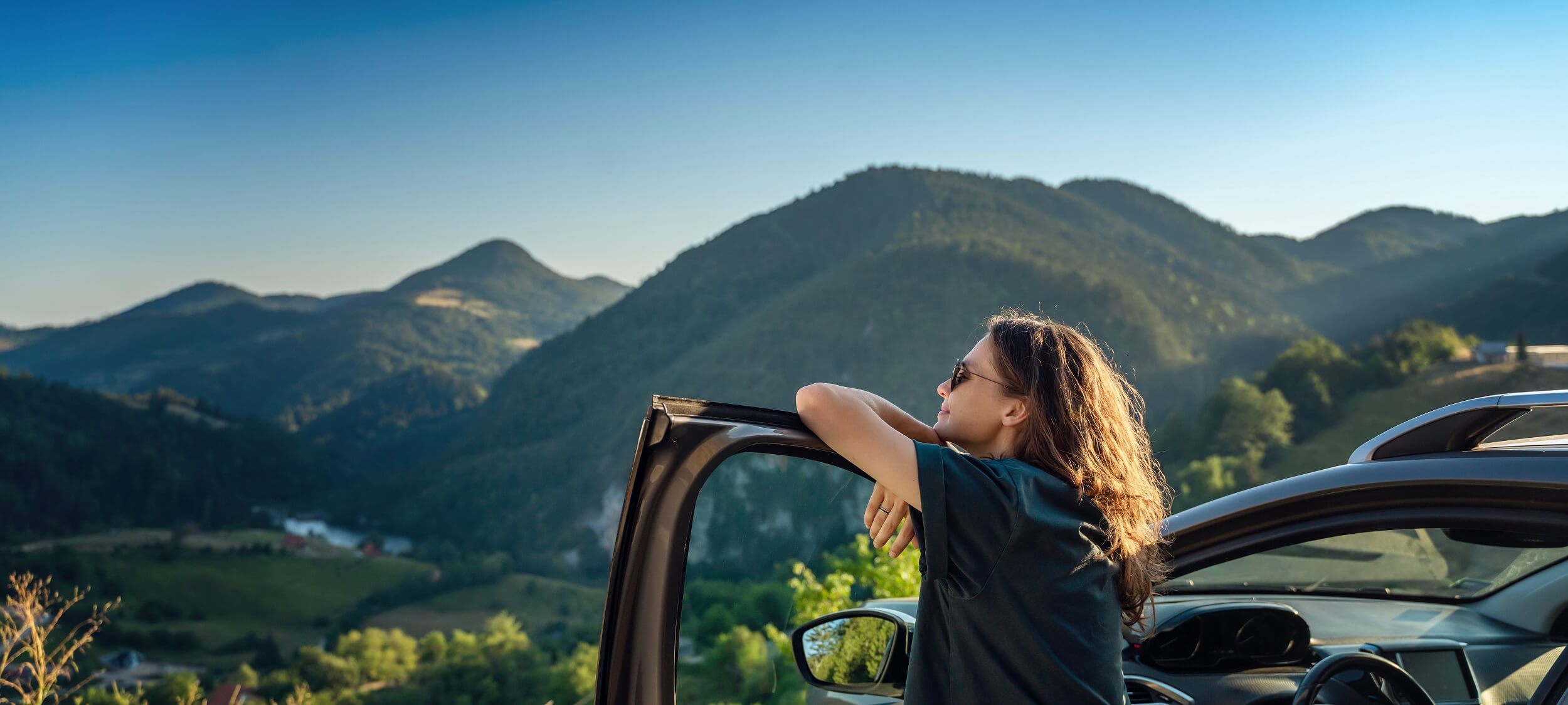 Frau lehnt sich entspannt an ihr Auto von Arval mit Blick auf die Berge, Symbol für ein sorgloses Auto Abo