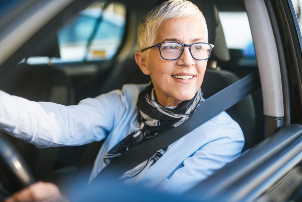 Une femme âgée conduit une voiture Arval et regarde devant elle avec satisfaction.